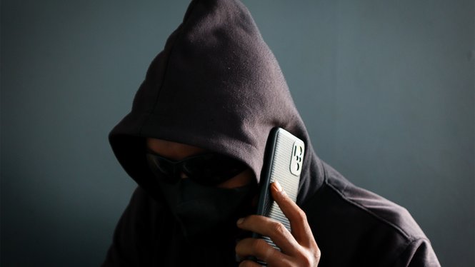 Home Person in Kapuzenpullover und Maske telefoniert verdeckt