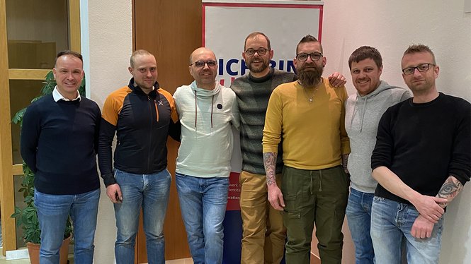 Home Sieben Männer stehen vor einer Tür und einem Banner in Innenraum