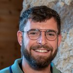 Unterland Lächelnder Mann mit Brille und kurzem Bart vor steiniger Wand