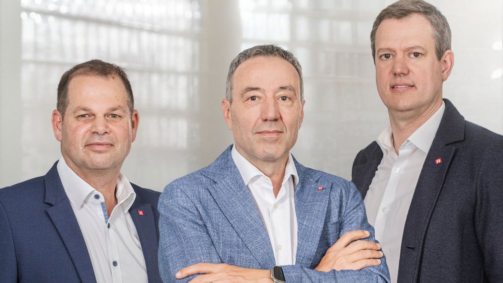 Home Drei Männer in Anzügen posieren vor hellem Hintergrund