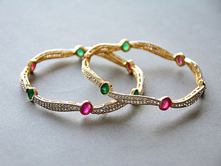 Percorso formativo Due braccialetti d'oro con pietre preziose rosse e verdi su sfondo grigio