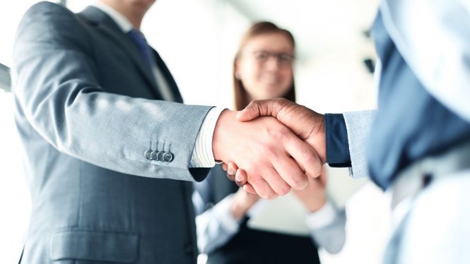 Home Zwei Geschäftsleute geben sich die Hand, eine Frau im Hintergrund lächelt