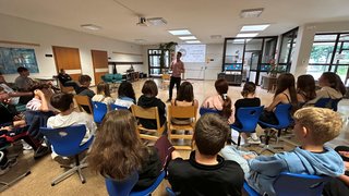 News Jugendliche sitzen in einem Raum und hören einem Sprecher bei einer Präsentation zu