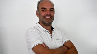 News Mann mit weißem Poloshirt lächelnd mit verschränkten Armen vor weißem Hintergrund