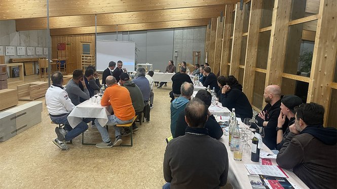 Home Menschen sitzen an Tischen in einem Holzraum und hören einer Präsentation zu