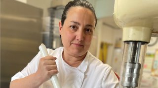 News Frau in weißer Kochjacke rührt mit großem Stab in Metallbehälter in Küche