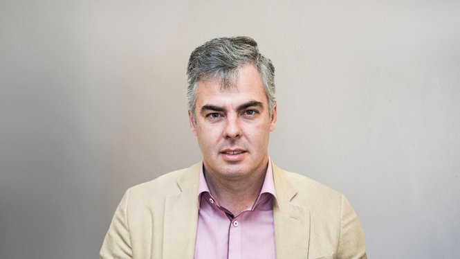 Home Porträt eines Mannes mit grauem Haar in beigem Sakko und rosafarbenem Hemd vor hellem Hintergrund