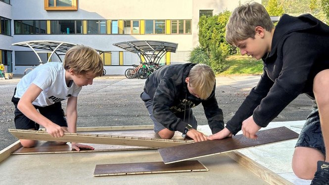 Home Drei Jugendliche setzen draußen gemeinsam Holzplatten auf einem Gestell zusammen
