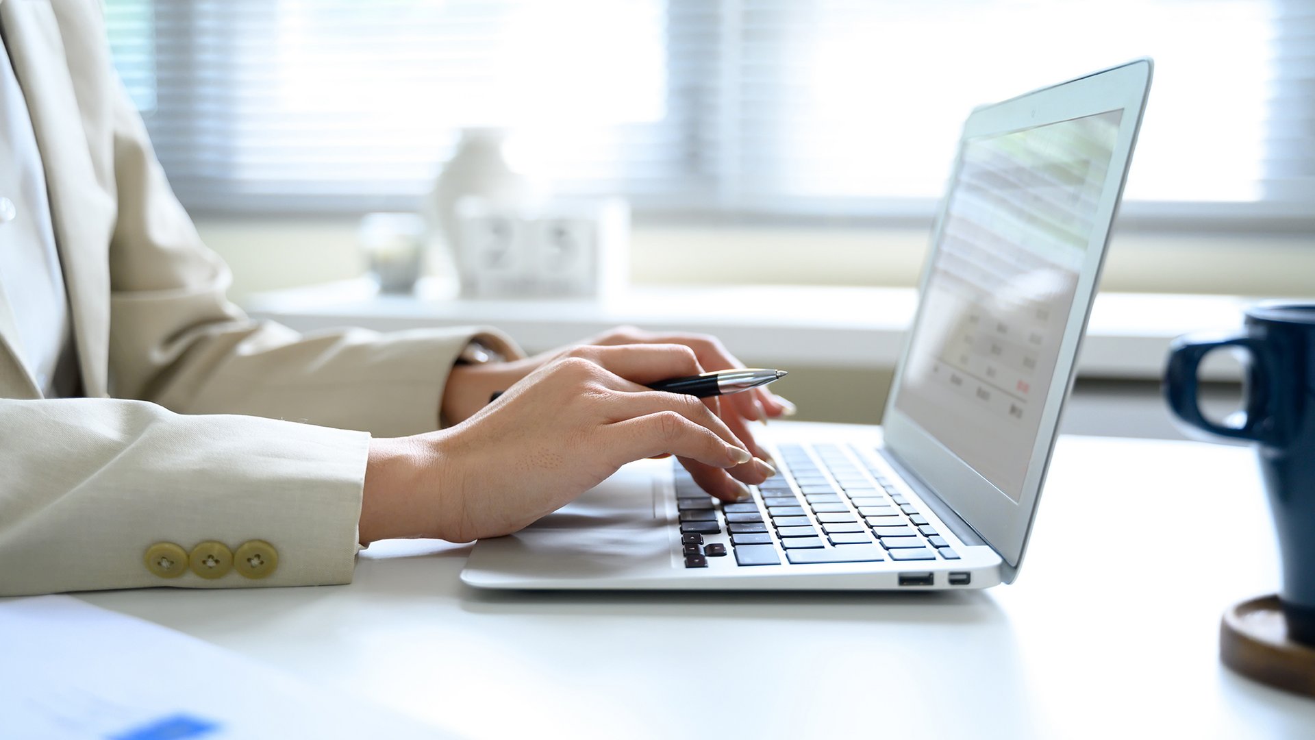 Home Person tippt auf Laptop-Tastatur mit einem Stift in der Hand am weißen Schreibtisch