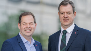 News Due uomini in abiti sorridenti davanti a uno sfondo sfocato