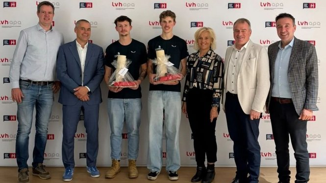 Home Sieben Personen vor einer Logowand, zwei junge Männer halten jeweils eine Trophäe