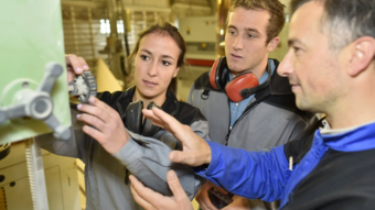 Home Drei Menschen arbeiten gemeinsam an einer Maschinensteuerung in einer Werkstatt