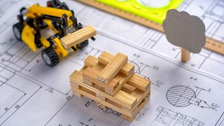 News Spielzeug-Bagger hebt Holzblöcke auf Bauplan mit Lineal und Baumfigur