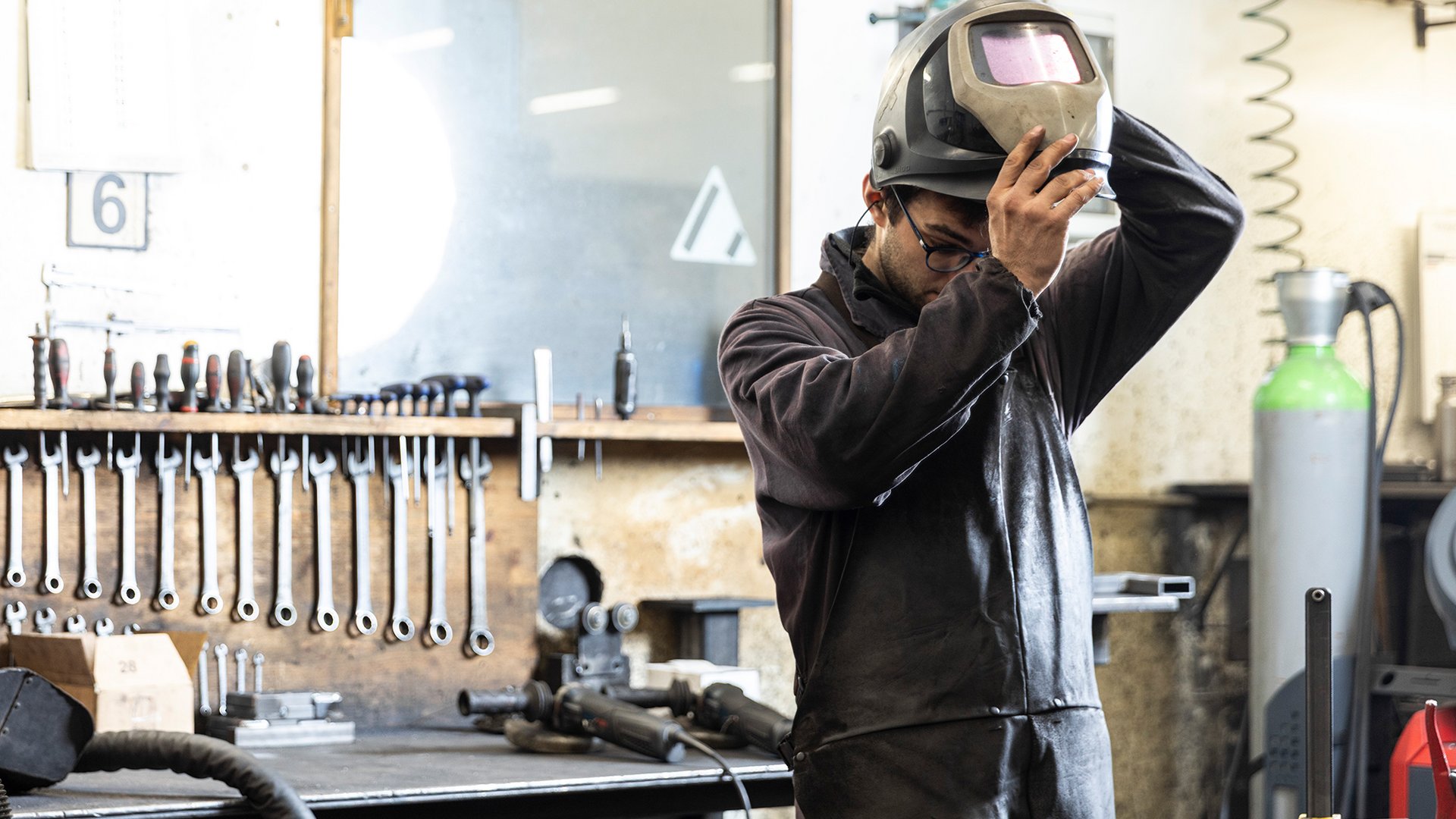 Home Handwerker hebt Schutzhelm in Werkstatt mit Werkzeugen an Wand