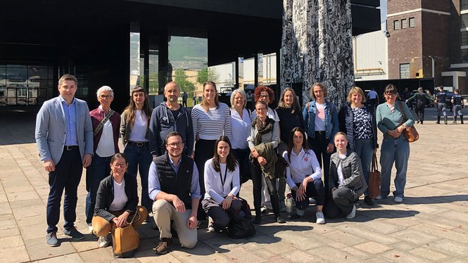 Home Gruppenfoto von 19 Menschen vor modernem Gebäude mit Kunstwerk