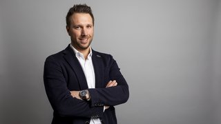 News Ritratto di uomo sorridente con le braccia incrociate su sfondo grigio