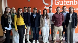 News Gruppe von elf Personen steht vor orangefarbener Wand mit Gutenberg Logo