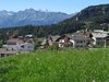 Home Bergdorf mit Kirche und grünen Wiesen vor Alpenkulisse bei klarem Himmel