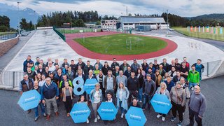 News Grande gruppo di persone con cartelli davanti a struttura sportiva sotto cielo nuvoloso