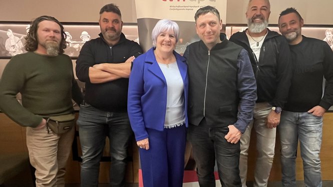 Home Sechs Personen stehen zusammen vor einem lvhapa Banner in einem Innenraum