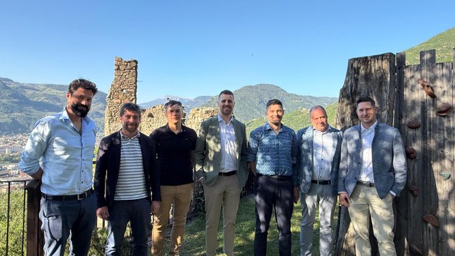 Home Sieben Männer stehen vor einer Burgmauer in einer Berglandschaft bei klarem Himmel