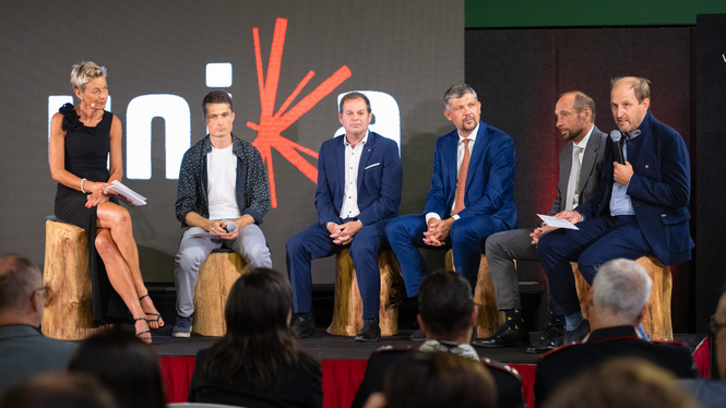 Home Podiumsdiskussion mit sechs Personen auf einer Bühne vor Publikum