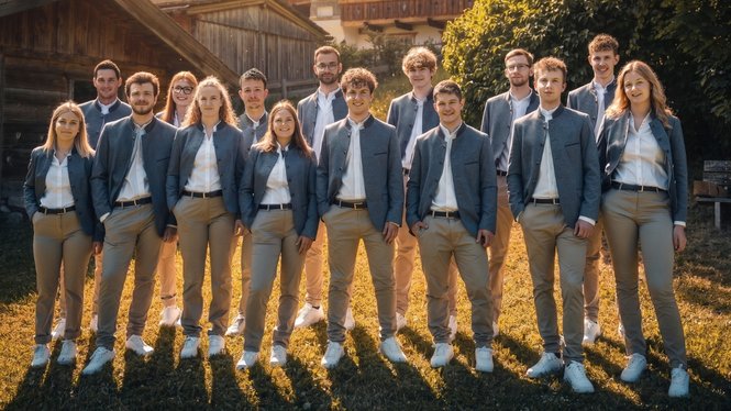 Home Gruppe junger Menschen in einheitlicher Kleidung steht draußen auf Gras im Sonnenlicht