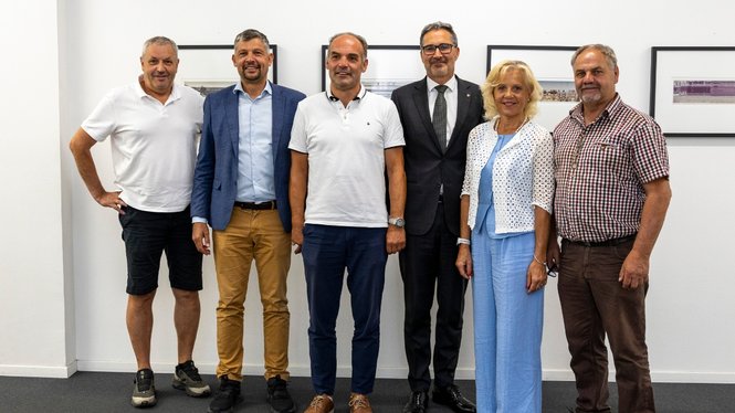 Home Sechs Personen stehen nebeneinander vor einer weißen Wand mit gerahmten Bildern
