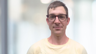 News Porträt eines lächelnden Mannes mit Brille vor unscharfem Hintergrund