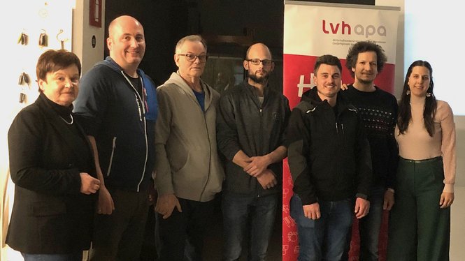 Home Gruppe von sieben Menschen steht vor lvhapa Banner in einem Raum