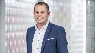 News Mann in blauem Anzug vor Glasbausteinwand lächelnd