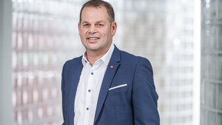 News Uomo in abito blu sorridente davanti a parete di vetro