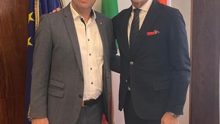 News Due uomini in abiti sorridono davanti a tre bandiere in una stanza interna