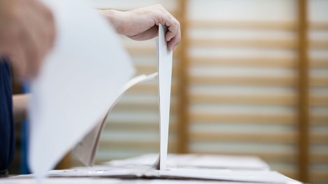 Home Eine Person wirft einen Stimmzettel in eine Wahlurne