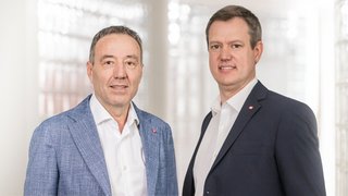 News Zwei Männer in Anzügen vor einem hellen, modernen Hintergrund