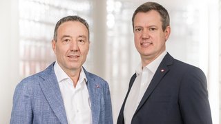 News Zwei Männer in Anzügen vor einem hellen, modernen Hintergrund