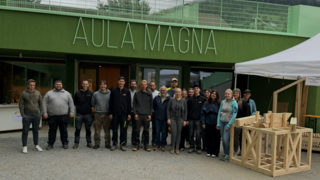 News Foto di gruppo davanti all'edificio Aula Magna con oggetto in legno sotto tenda