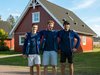 Home Drei junge Männer mit blauen Jacken posieren vor einem roten Haus im Freien