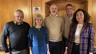 News Cinque persone stanno in piedi davanti a una parete di legno in una stanza accogliente