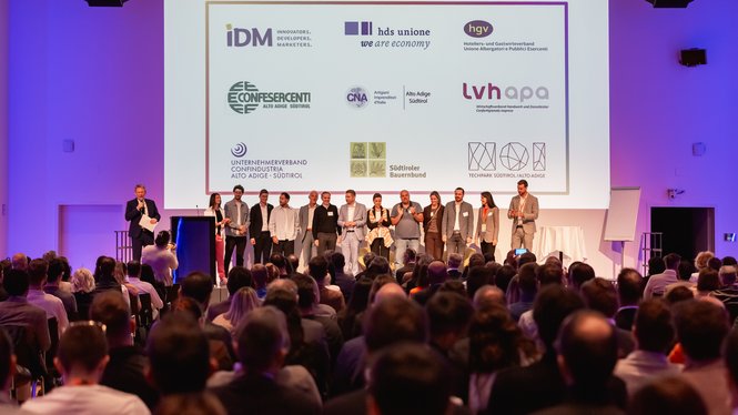 Home Gruppe auf einer Bühne vor Publikum und einer Leinwand mit Partnerlogos