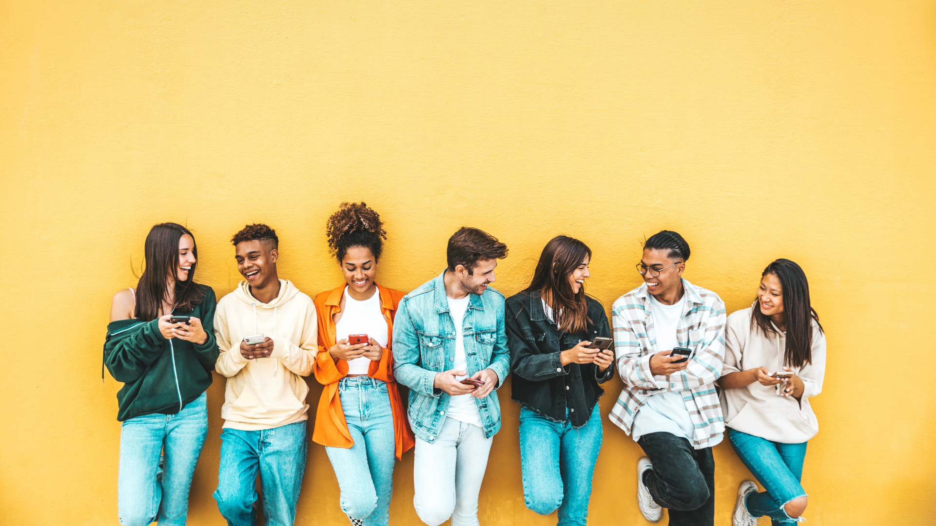 Home Junge Menschen lehnen an gelber Wand und benutzen Smartphones