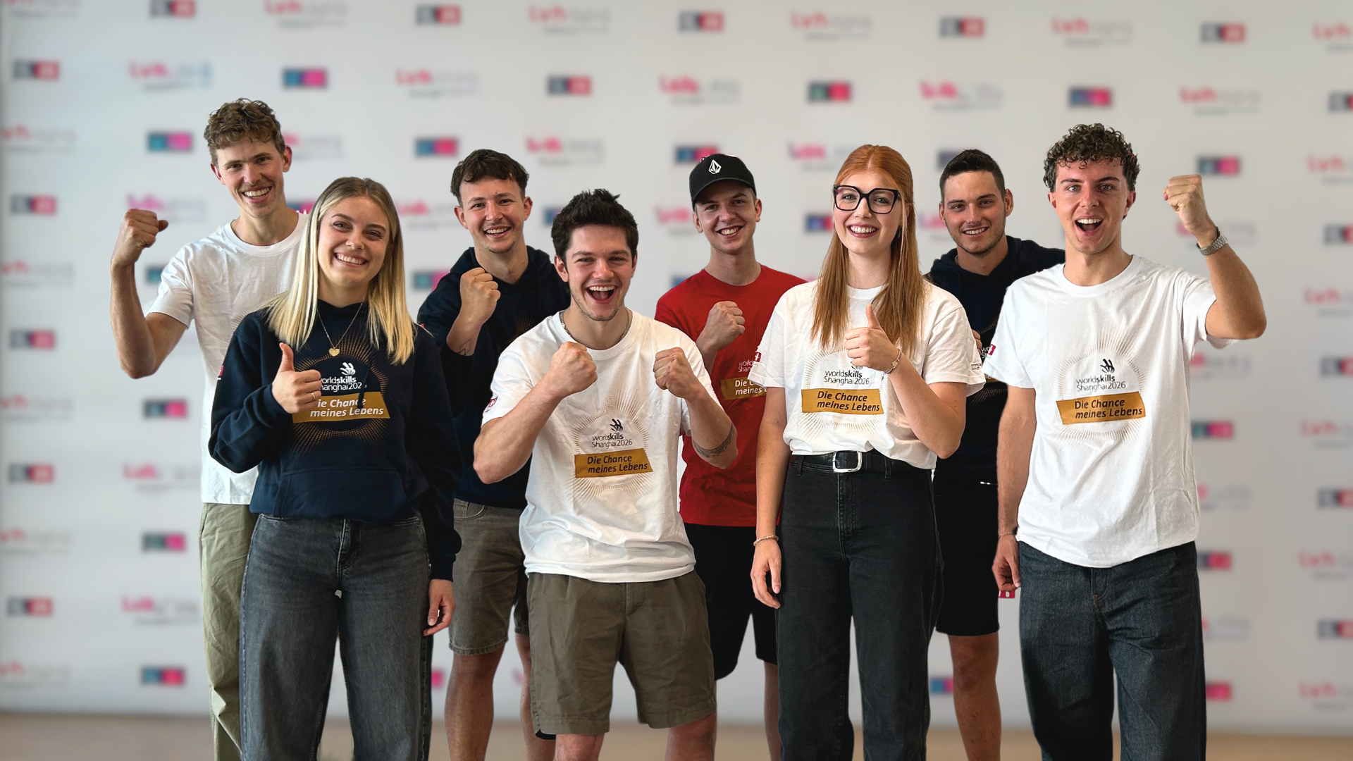 Home Acht lachende Menschen in bedruckten T-Shirts posieren gemeinsam vor einer Fotowand